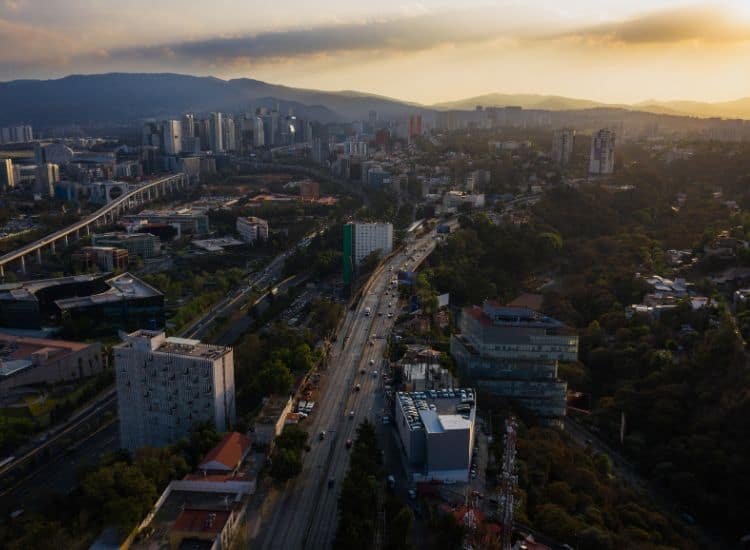 Vista aérea de la alcaldía Álvaro Obregón, mostrando una mezcla de zonas residenciales y comerciales con edificios modernos y áreas verdes circundantes. En el fondo se pueden apreciar las montañas que rodean la zona.